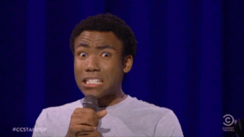 Animated GIF of a man on stage holding a microphone, making an exaggerated wincing 'yikes' face.